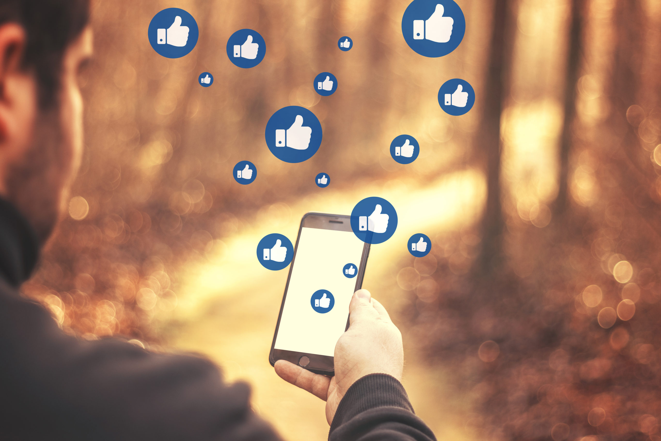 Young man watching Facebook on his smartphone during a walk in the forest - multitude of thumbs up like icons in speech bubbles - life style and social networks