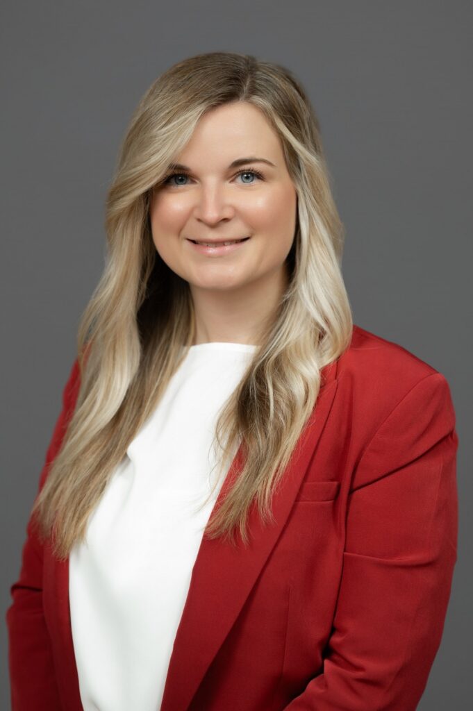 Headshot of a woman looking directly at the camera and wearing a white shirt and red blazer